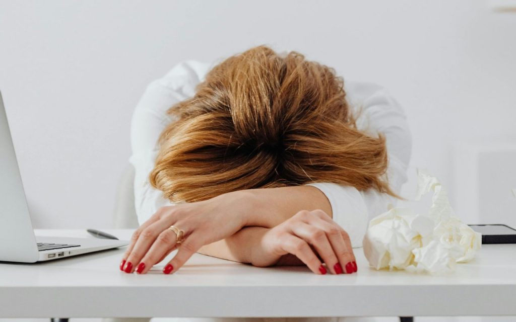 Osoba drži spuštenu glavu nad radnim stolom